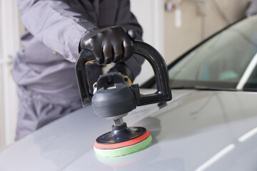 Man polishing car hood with orbital polisher indoors, closeup