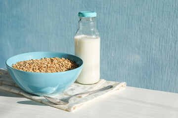 Tasty oatmeal in bowl and milk served on white wooden table against light blue background, space for text