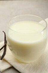 Glass of milk and vanilla pods on light grey table, closeup