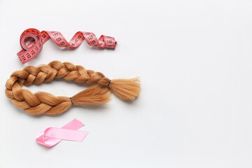 Braided red hair for donation with pink awareness ribbon and measuring tape on white background