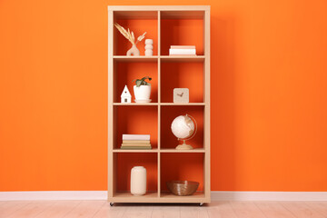 Wooden shelving unit with different home decor near orange wall indoors
