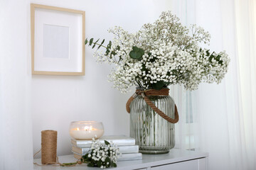 Bouquet of beautiful gypsophila flowers and eucalyptus branches in vase near decorative elements on...
