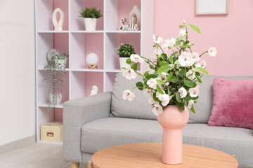 Stylish living room with cozy sofa, coffee table and bouquet of blooming tree branches