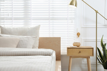Comfortable bed and nightstand in stylish room, closeup. Interior design