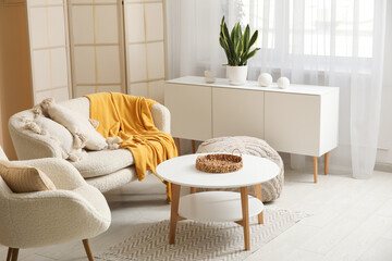 Modern interior of living room with sofa, chest of drawers, coffee table and armchair in living room