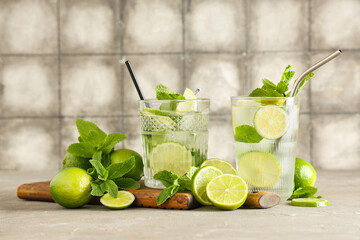 Glasses of fresh Mojito cocktail with limes and mint on grey table