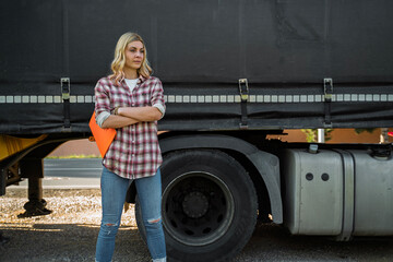 Young blonde woman truck driver with folder in her hands posing next to a truck, closeup shot