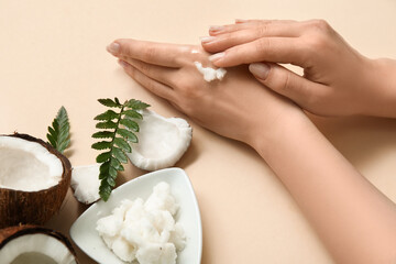 Young woman applying coconut oil on hands on beige background, closeup