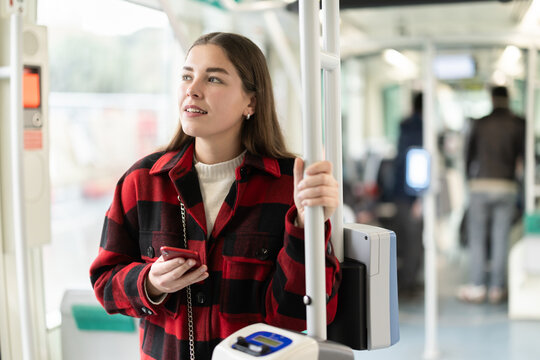 Young European woman rides a tram and prepares to get off at the stop she needs. Girl paid for the trip using an application on her mobile phone