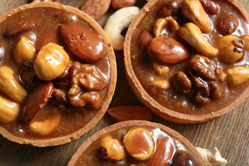 Tasty tarts with nuts and caramel sauce on brown wooden board