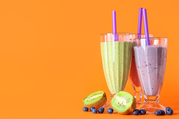 Glasses of different fresh smoothie with kiwi and blueberries on orange background