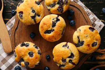 Napkin, wooden tray and tasty blueberry muffins on black wooden background, closeup