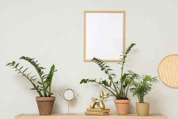 Books, statuette, mirror and different houseplants on wooden rack near light wall in living room