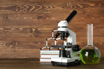 Modern microscope with chemical flask, books and molecular model on table against wooden background
