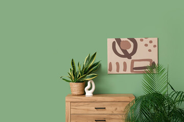 Painting hanging on green wall, chest of drawers and houseplants in room