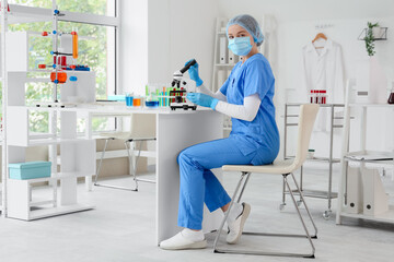 Female chemist with microscope sitting at table in laboratory