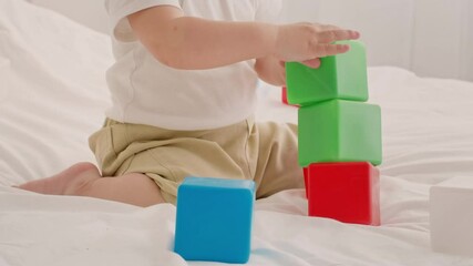 A young child joyfully stacks brightly colored blocks on a soft surface. The toddler focuses intently on balancing the blocks while playing in a cozy indoor setting during playtime.