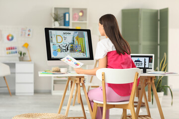 Young female graphic designer working at table in office, back view