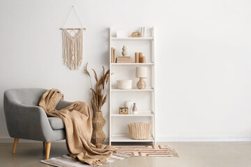 Interior of stylish modern room with armchair and shelving unit near beige wall