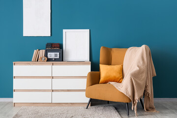 Interior of room with armchair, books, piggy bank and safe box on commode near blue wall