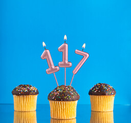 Birthday candle with the number 117 - Three cupcakes on a blue background