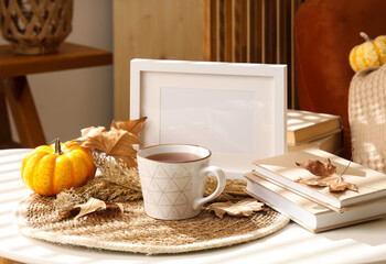 Coffee table with cup of hot tea, books, autumn leaves and pumpkin in living room