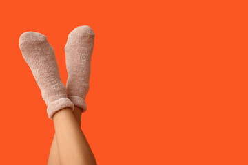 Legs of young woman in warm beige socks on orange background