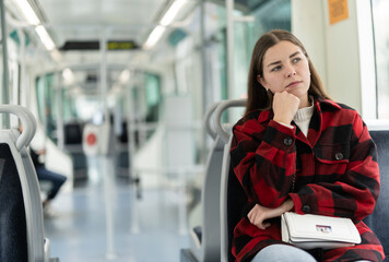 Obraz premium Young woman is driving home tired in public transport. Girl is sitting in a tram car