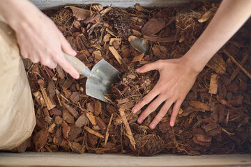 Hands mixing dried leaves in a compost bin
