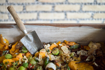 Fresh food scraps in a compost bin with gardening trowel