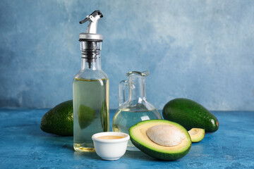 Ripe avocado, bottle and decanter of oil on color background