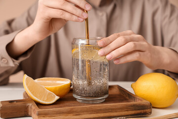 Woman adding straw into glass of water with chia seeds and lemon near table