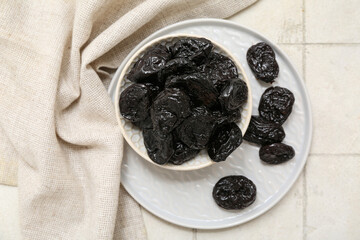Bowl and plate with dried prunes on white tile background