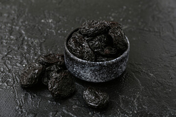 Bowl with dried prunes on black background
