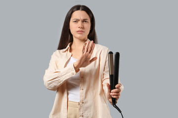 Dissatisfied young woman with hair straightener showing stop gesture on white background