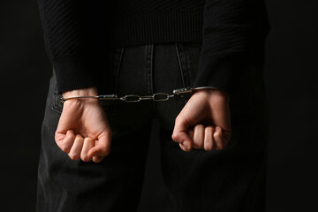Young woman in handcuffs on black background, back view