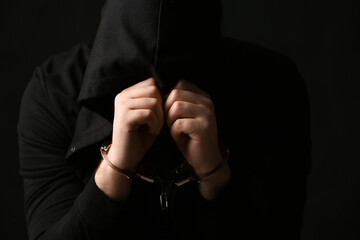 Young man in handcuffs closing face with hands on black background