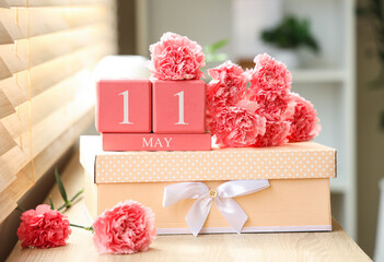 Cube calendar with date of Mother's Day, carnation flowers and gift box on shelf in room, closeup