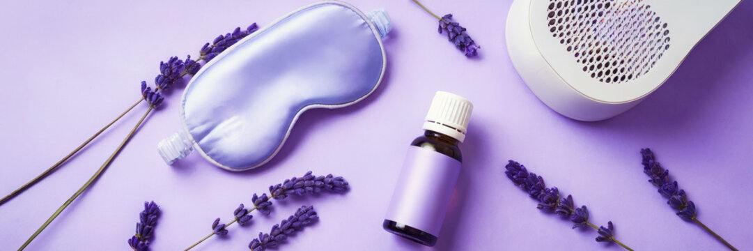 Biohacking concept for deep sleep, flat lay of bottle of lavender essential oil, sleeping mask with white noise machine on a purple background, long banner