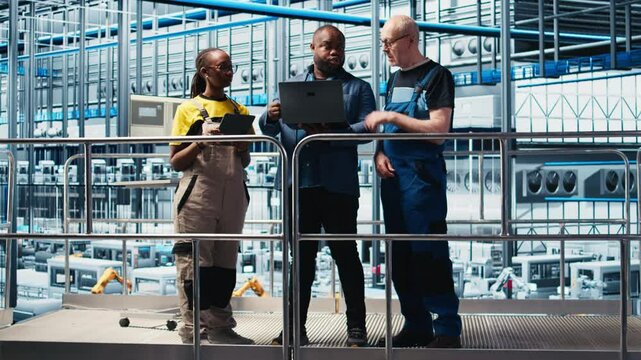 Smart factory manager discussing with employees automated workflow implementation. Supervisor overseeing industrial plant talks with workers, integrating sensors into production, camera A
