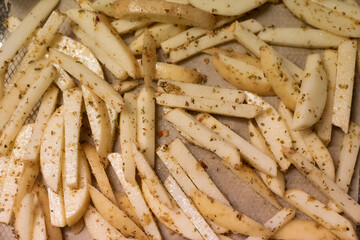 Top down view seasoned potato fries on a baking tray covered in brown paper, ready for the oven.