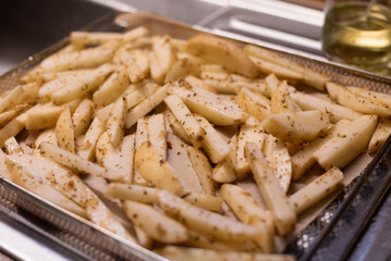 Closeup view of seasoned potato fries on a baking tray with oil in background, on kitchen sink, ready for the oven.
