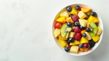 Overhead view of a fruit salad bowl filled with mixed fruits like pineapple chunks, blueberries, and mango slices, against a minimalist white backdrop.