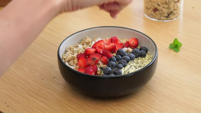 Preparation of a delicious granola bowl with fresh berries and chia seeds on a wooden table