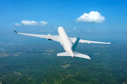 Commercial passenger jet airliner gains altitude after takeoff from a departure airport over green fields and forests high in the sky