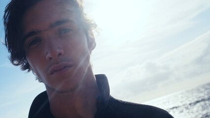 Young man with blown brown hair against the blue sky on summer sunny day. Stylish man in black...