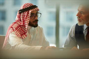 Middle Eastern and Caucasian male managers discussing business project at work in modern office, medium closeup