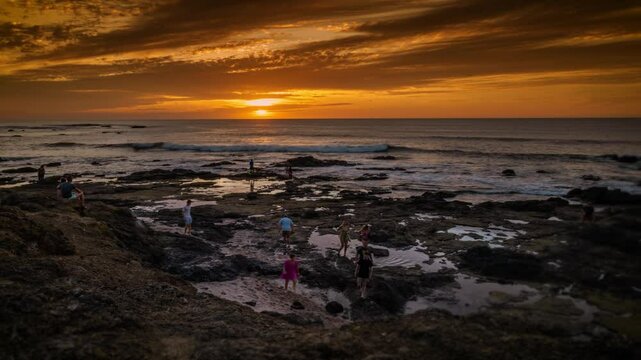 rocky coastline time lapse with setting sun and open ocean and long exposure people moving around the coast