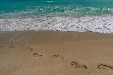 Turquoise sea water wave motion. Foot steps on sand. Calm sea. Seaside resort. Bright sky and waves on beach. Beautiful foamy shoreline. Sea background. Blue ocean. Sandy ocean beach. Sea waves.