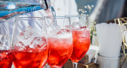 The bartender pours soda into a glass of wine with ice in close-up. Creating a red cocktail, wine, juice, liqueur, bubbling water. Refreshing cocktail in summertime. Beach bar, sun, cold drinks